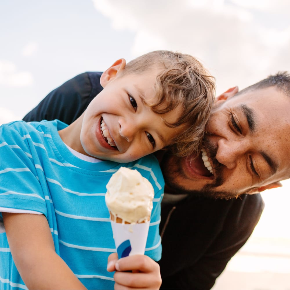 Boy with an ice cream cone standing in front of his father and laughing. Maybe not sharing any of his ice cream with dad.