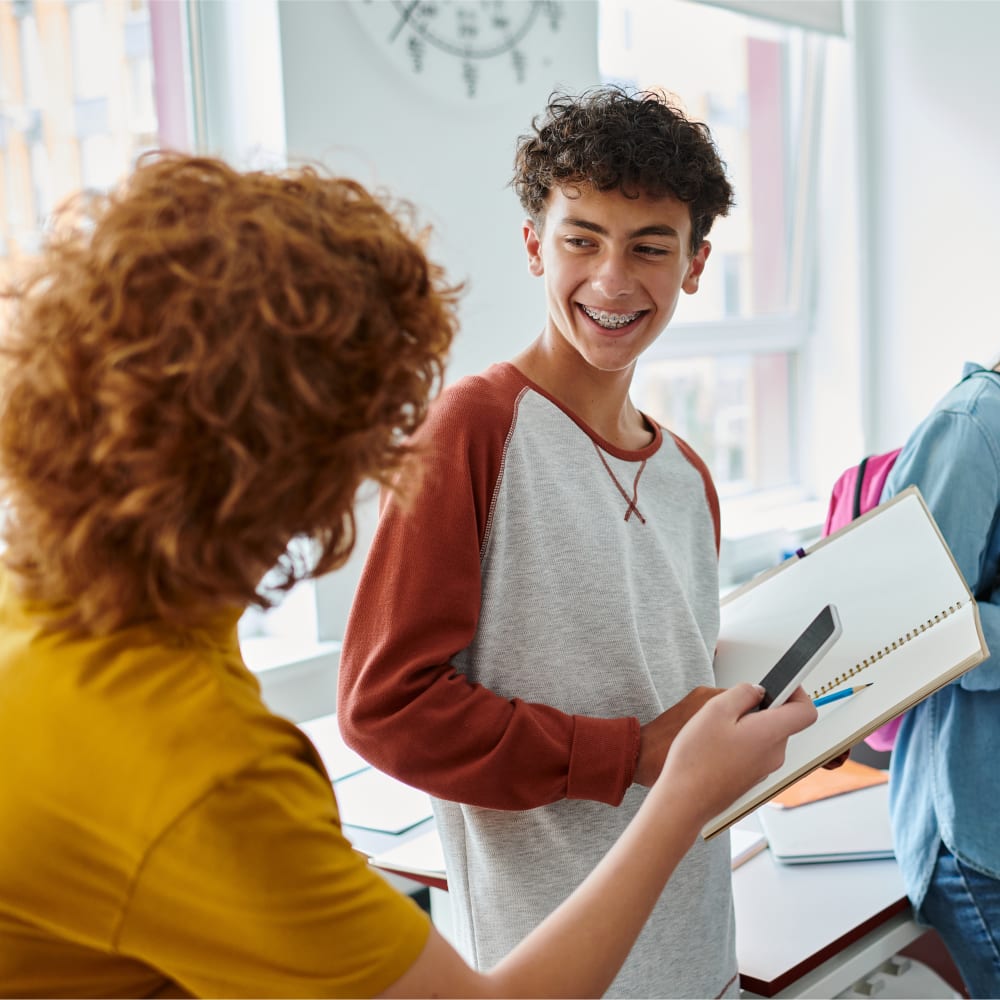 Two people with curly hair are standing together and the young boy is smiling, revealing his braces.