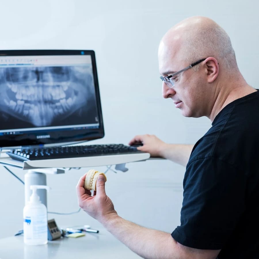 A dentist and a patient review the patient's oral health. A screen shows a digital rendering of her upper teeth.