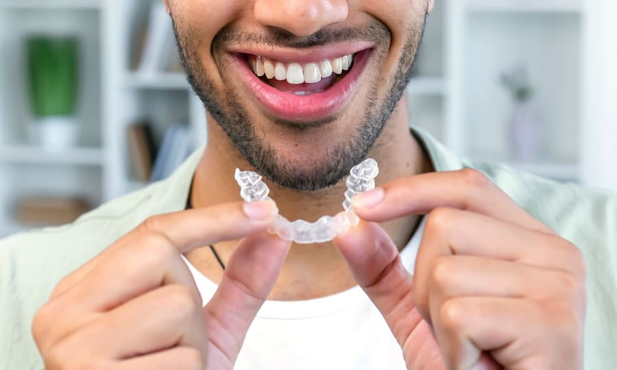 A smiling man holds a clear aligner near his mouth.