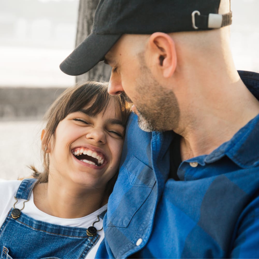 A father with his arm around his daughter who is smiling and laughing at him.