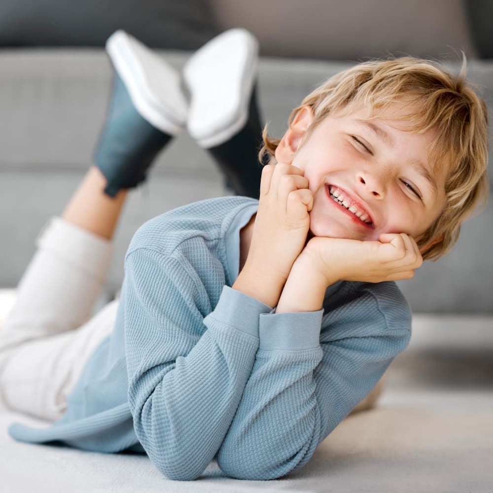 Smiling young boy laying on the floor with his chin resting in his hands.