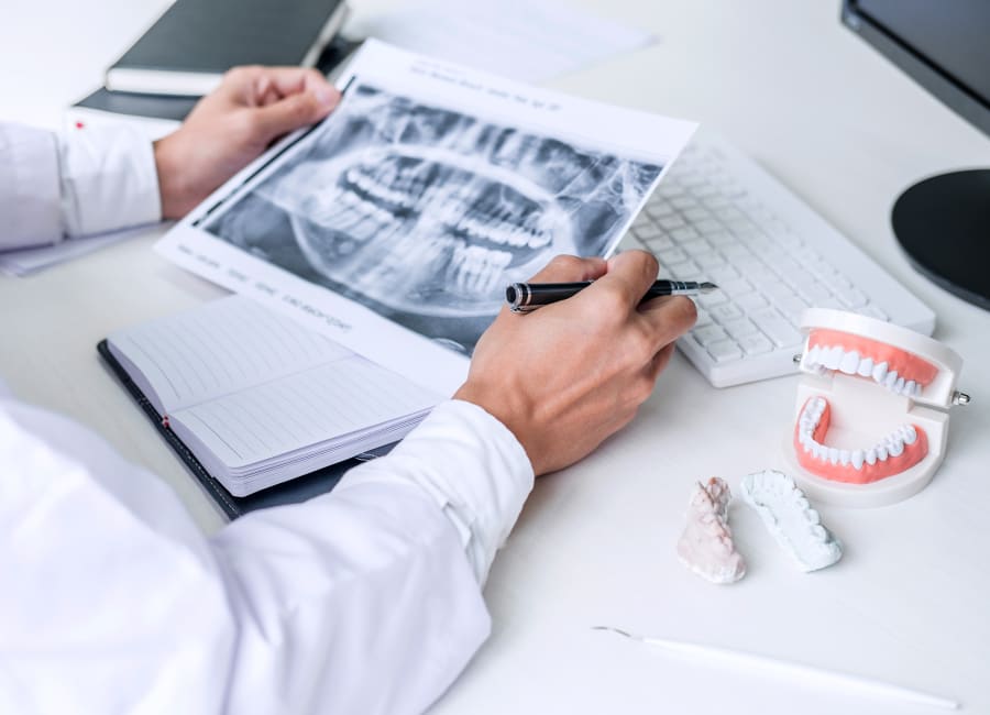 A dental professional reviews a patient's printed digital X-rays at their desk.